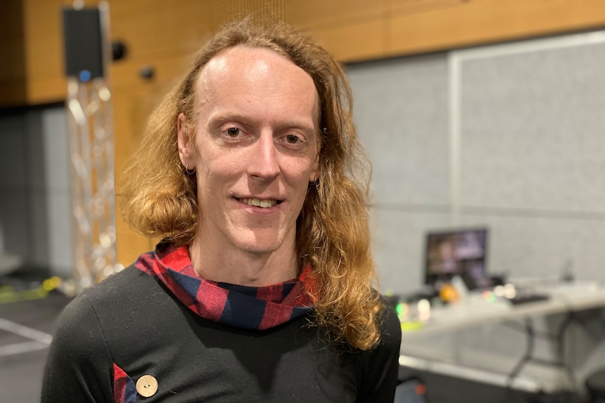 A person with red hair and a black top stands smiling at the camera.