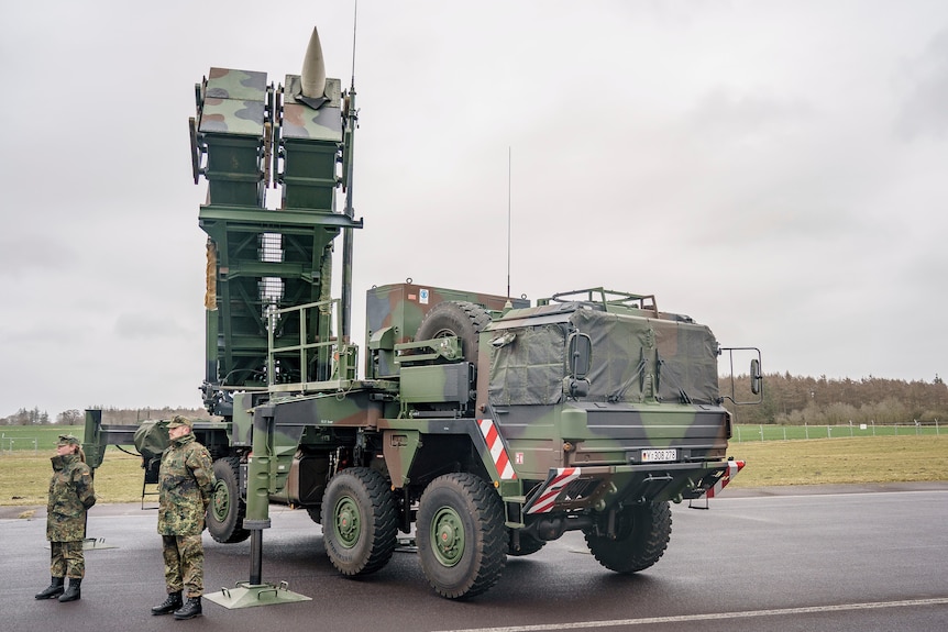 Two Russian soldiers stand in front of a Patriot missile system. 