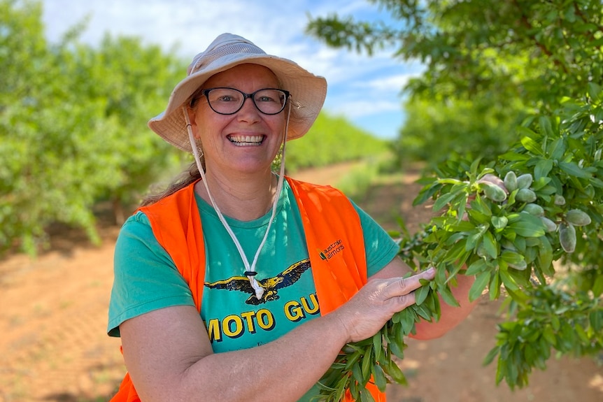 A woman in wearing a hat standing next to an almond tree.