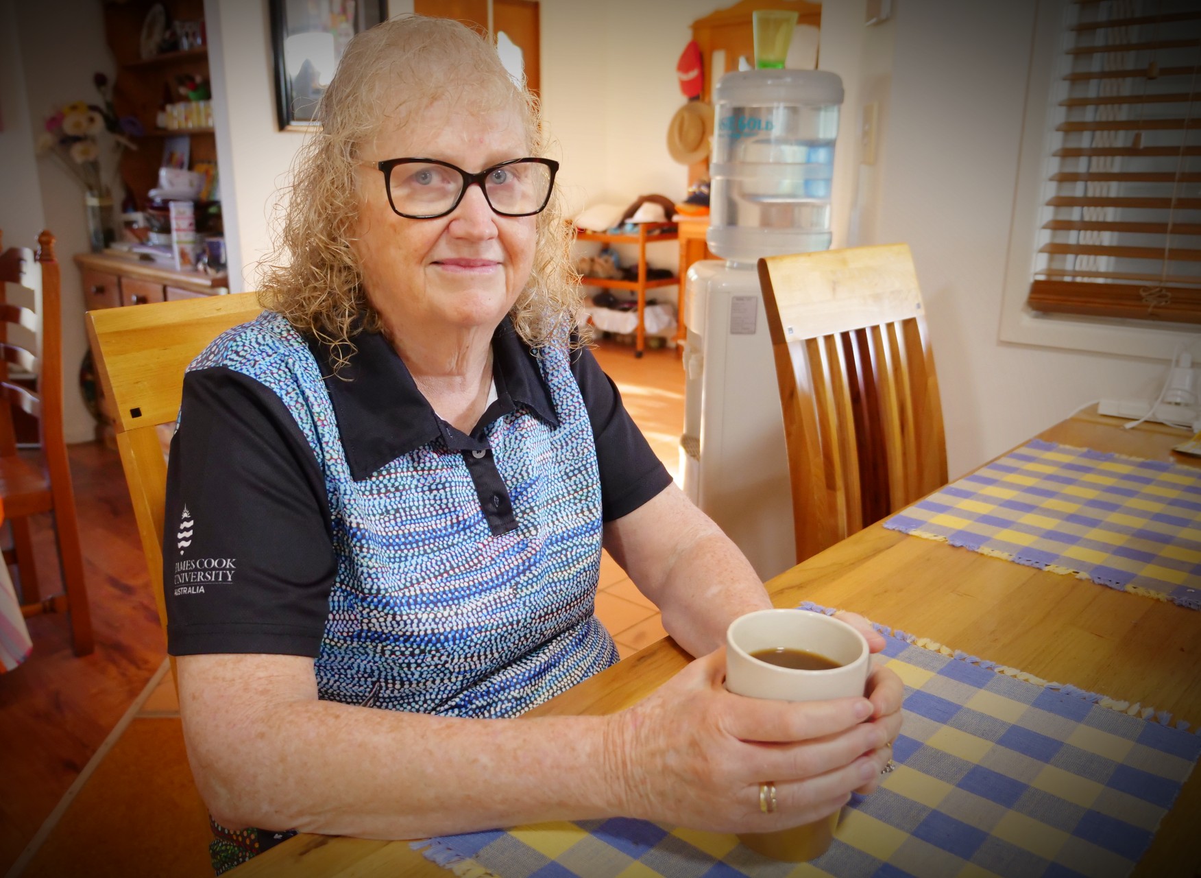 Woman with glasses sitting at a table with a cup of tea looking at the camera