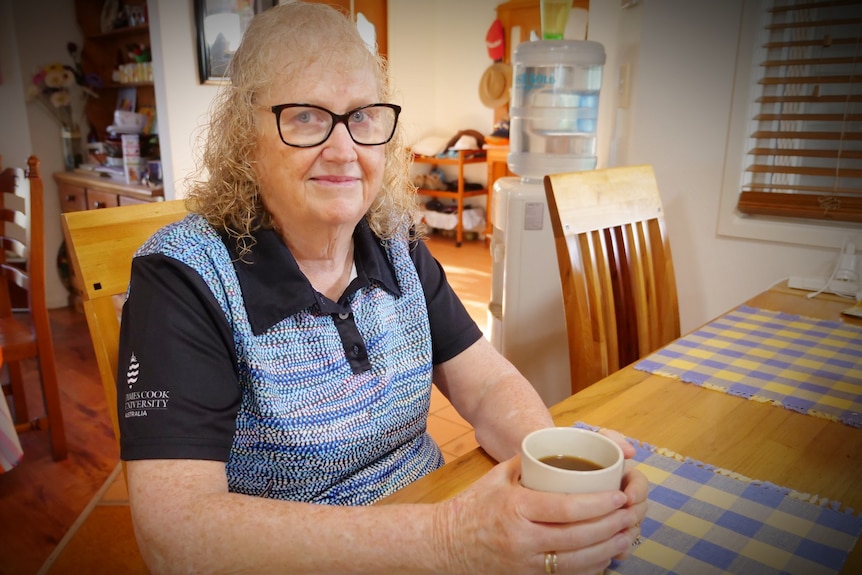 Woman with glasses sitting at a table with a cup of tea looking at the camera