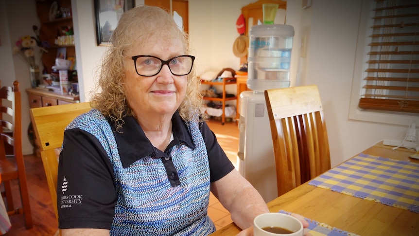 Woman with glasses sitting at a table with a cup of tea looking at the camera