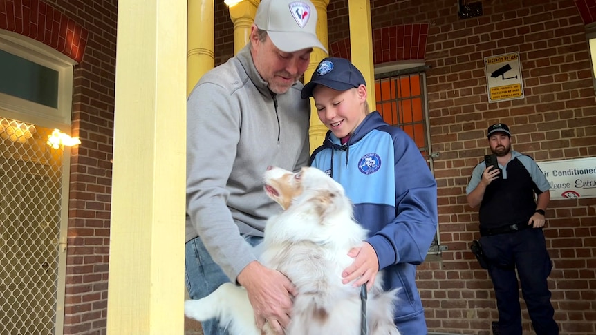 Dad, son and dog all hugging in front of a police station, they're smiling