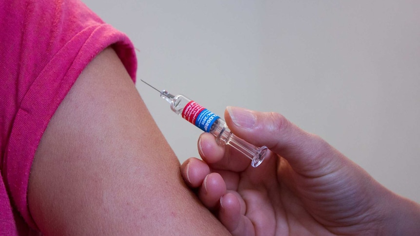A doctor holds a needle close to the arm of a patient.