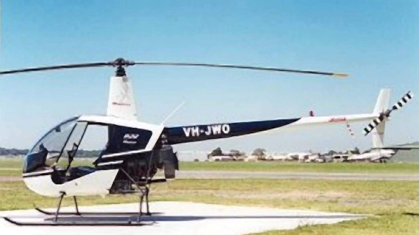 A Robinson R22 helicopter sits on a helipad on a clear, sunny day, with no one in the cockpit