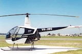A Robinson R22 helicopter sits on a helipad on a clear, sunny day, with no one in the cockpit
