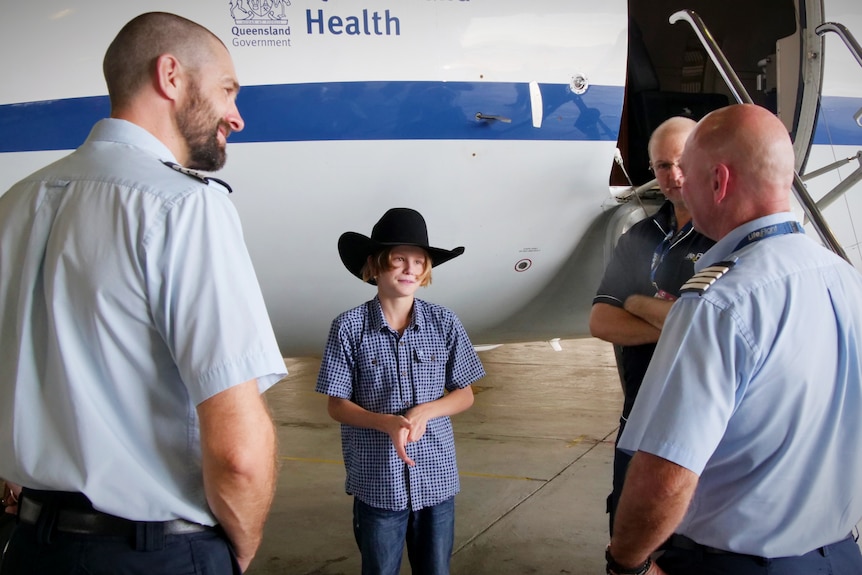 A boy in a cowboy hat speaks to an emergency rescue crew beside a small aircfraft.