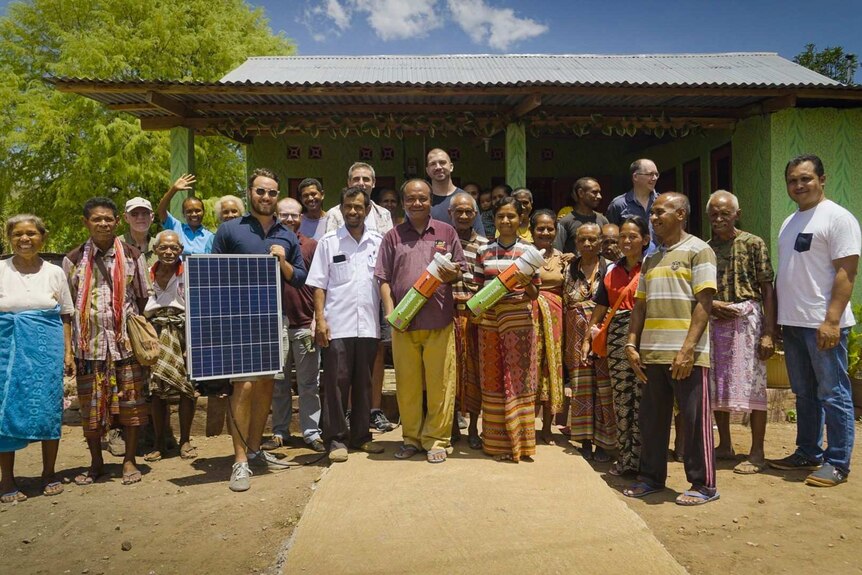 A group of people hold a solar panel and an energy charger.