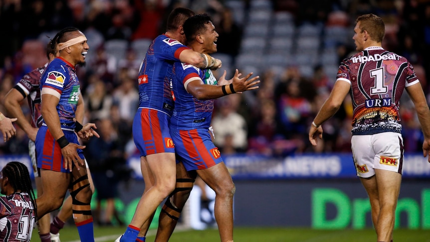 Daniel Saifiti is hugged by Newcastle Knights teammates after a try in their NRL clash against Manly Sea Eagles.