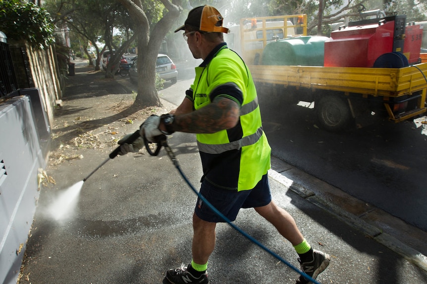 A worker uses a high pressure cleaner on a footpath