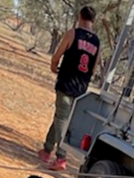 The back of a man walking away from a trailer. He is wearing a black and red basketball singlet.