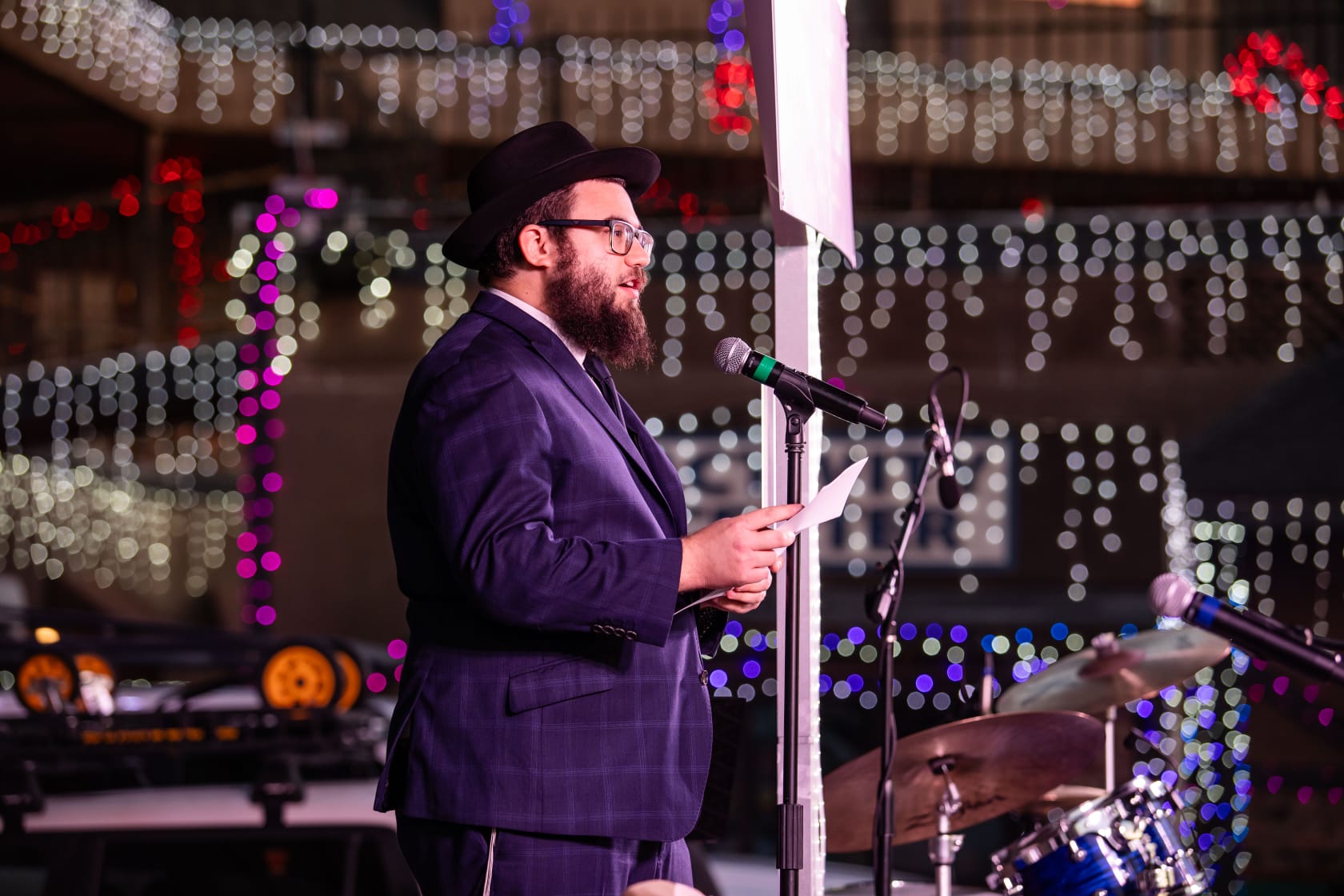 Rabbi Super se para frente a luces de colores y habla por un micrófono.