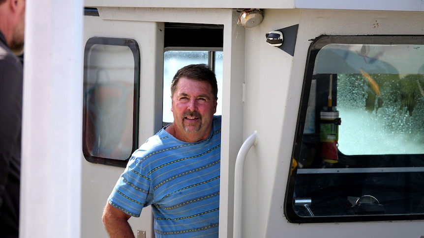 Picture of Wayne Cripps leaning out of the cabin door on his boat. Wayne is smiling and looking away from the camera.