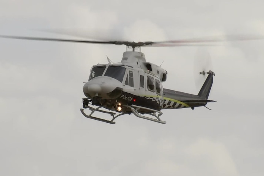 A police helicopter in the air with grey sky behind