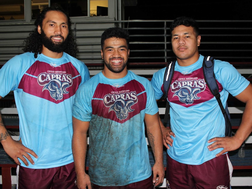 Three rugby league players standing next to each other, wearing blue jerseys
