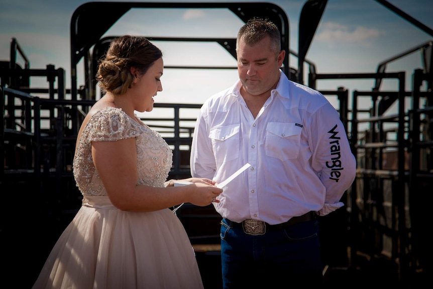 A bride and groom stand in front of the main gate in a rodeo ring as the bride reads her vows.
