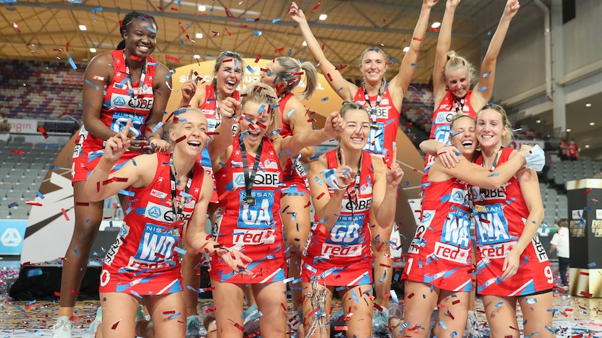 Swifts players throw red and blue confetti in the air and pose with their medals and trophy
