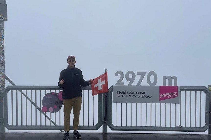 Chris Ross points to the Swiss flag and a sign that says 2970m on top of some railings.