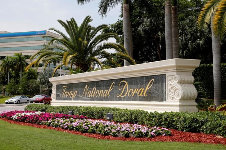An entrance sign to the Trump National Doral is seen set behind grass with pink white and fuchsia flowers in front.