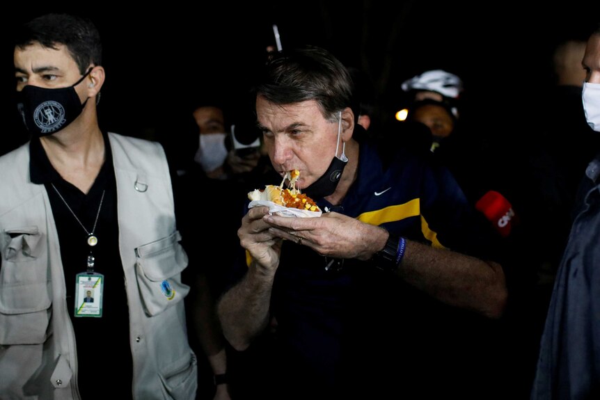 Jair Bolsonaro eats a hot dog while surrounded by body guards