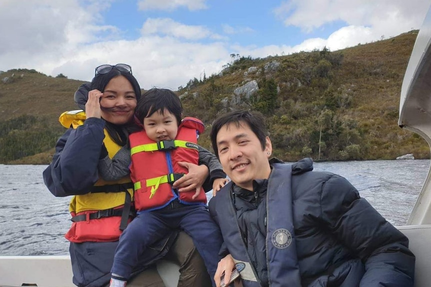 Two Asian adults and their child wear lifejackets on a boat