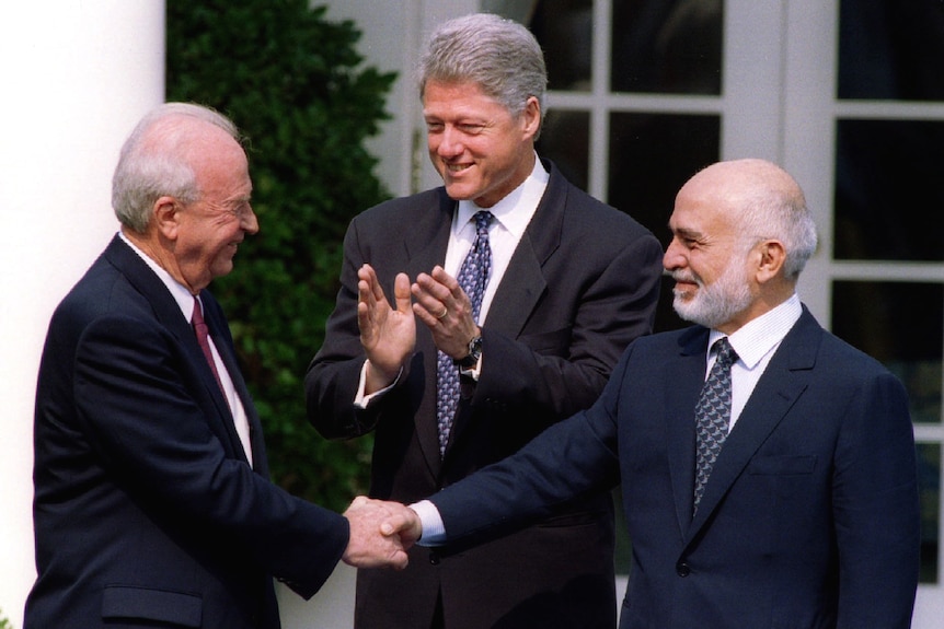 Yitzhak Rabin and King Hussein shake hands while Bill Clinton claps.