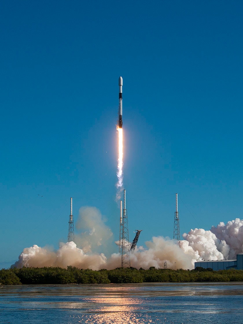 Rocket launches into a blue sky, headed for space, fire burning underneath.