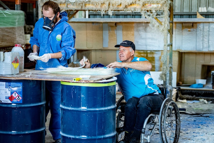 Andrew Meddings in a wheelchair looking through some material with a work colleague, who is wearing a gas mask