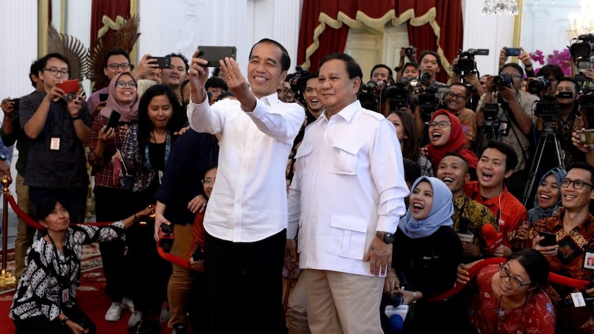 Indonesian President Jokowi and Prabowo Subianto take a selfie in front of a crowd of young people.