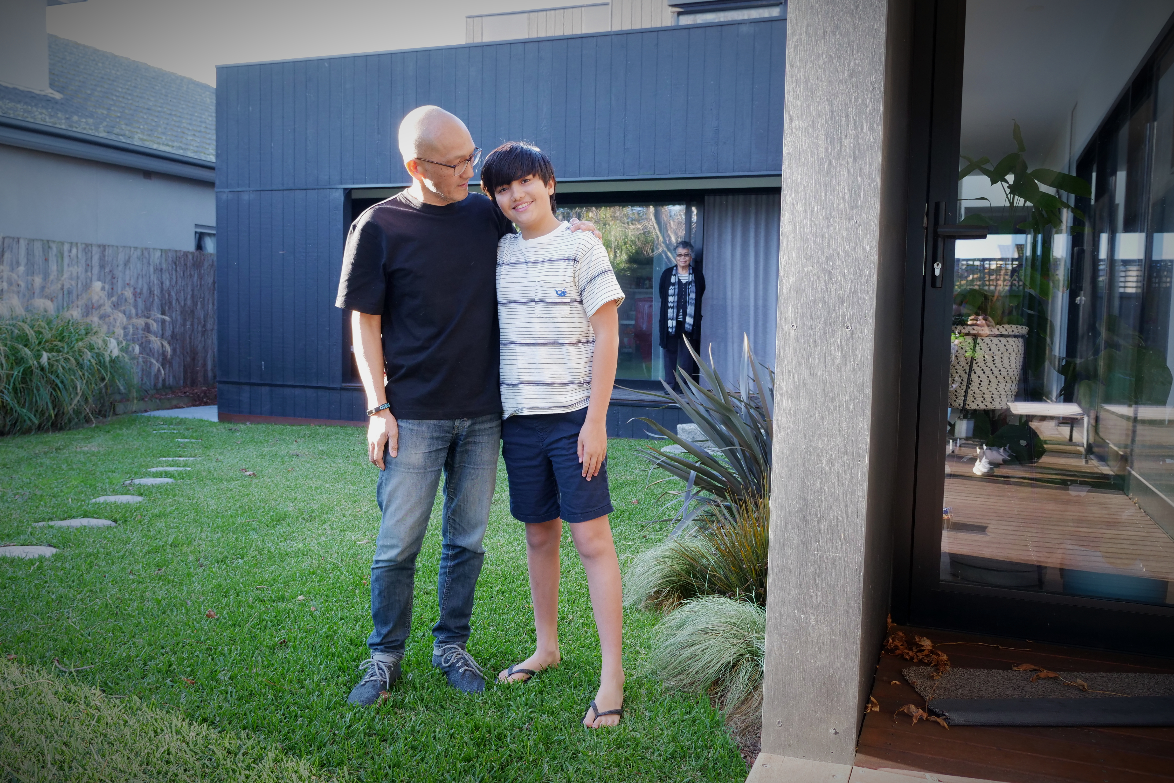 一个男人和一个男孩并排站在绿草地上，讲述了一个关于多代家庭住宅设计的故事。 “ class=