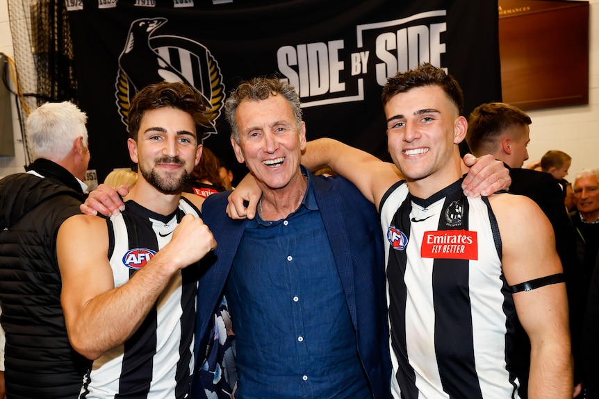 Peter Daicos stands arm in arm with Josh and Nick Daicos in the Collingwood rooms