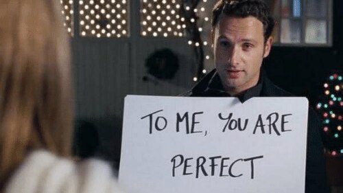 A man holding a cardboard sign saying 'To me you are perfect' from the movie Love Actually.