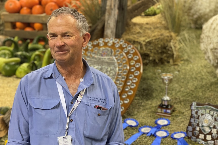 A grey-haired man in front of trophies and farm produce.