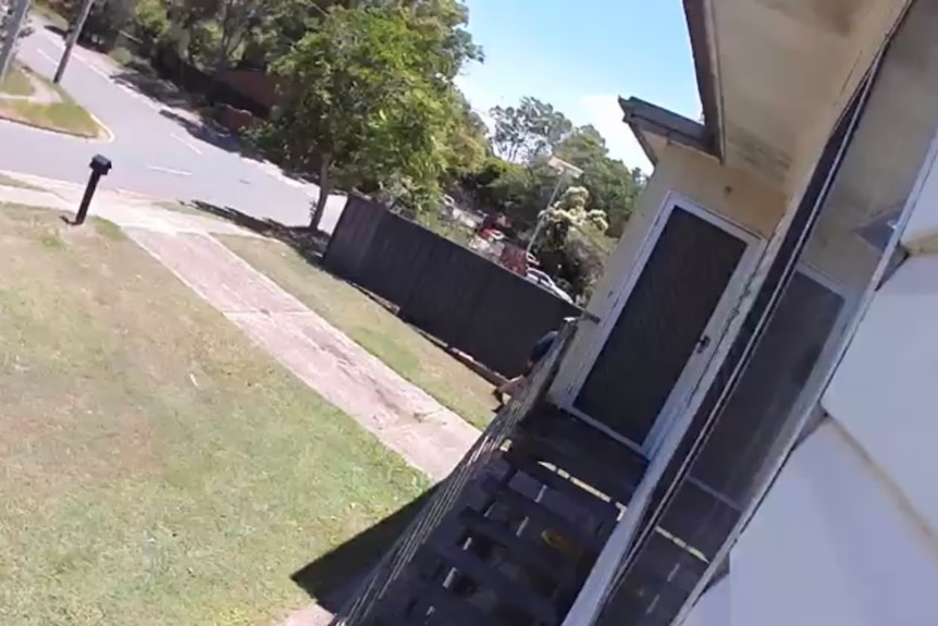 A still frame from home security camera footage of a man walking down the side of someone's home.