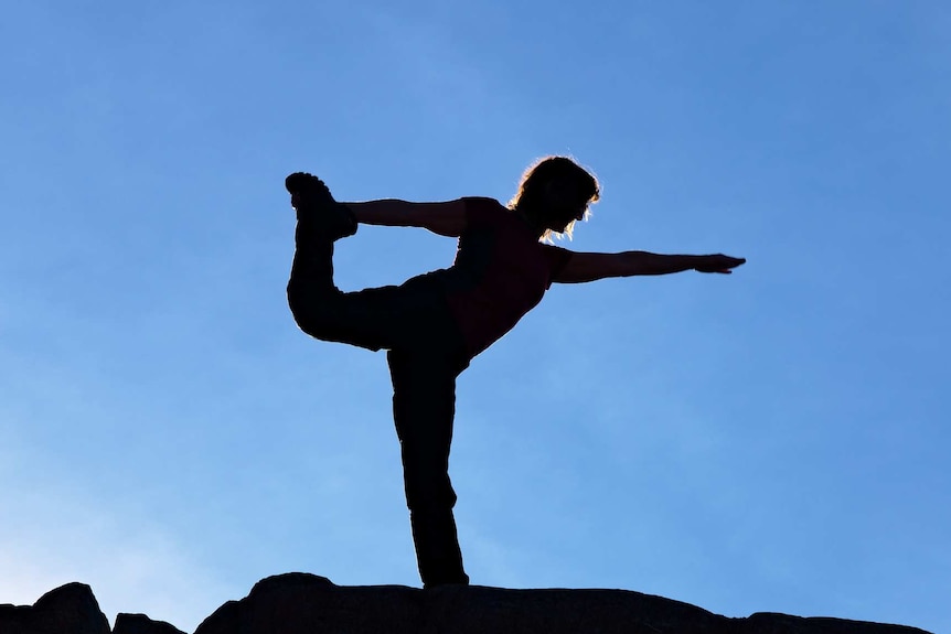 A silhouette of person in a standing triangle yoga pose.