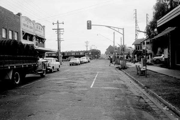 A black and white photo of a woman crossing a road in 1969 with some vehicles lined up.
