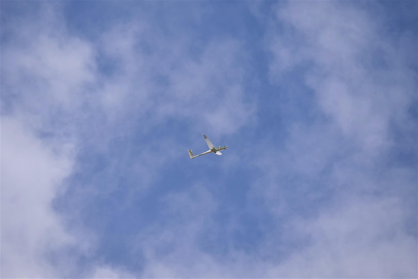 A small plane is visible in a blue sky with wispy white clouds.