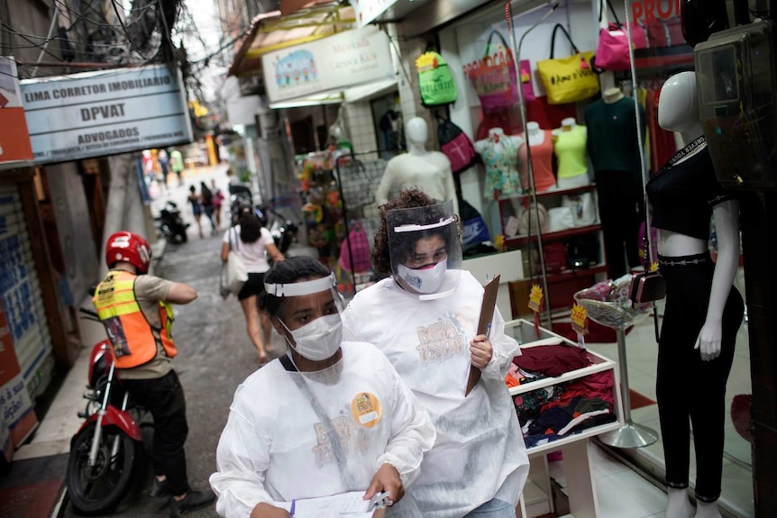 Health workers in protective clothing and equipment walk through the Rocinha slum to test people for COVID-19