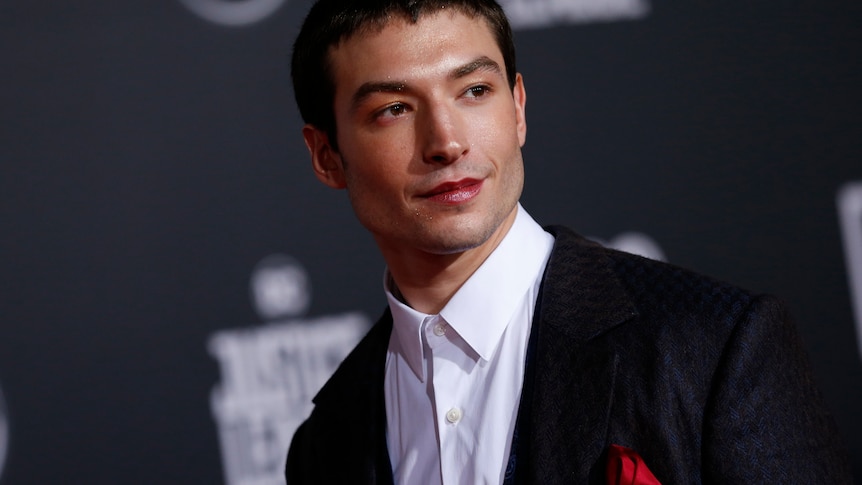 A person with close cut dark hair wears a suit and smiles to the side of camera