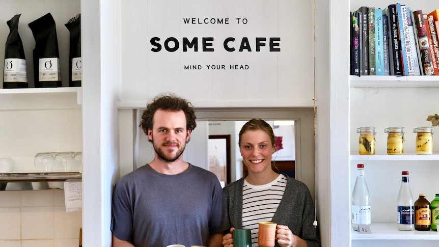 A man and a woman holding coffee mugs, standing in front of a door in cafe