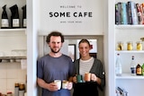 A man and a woman holding coffee mugs, standing in front of a door in cafe