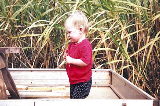 a young girl in the back of a ute against a cane field 