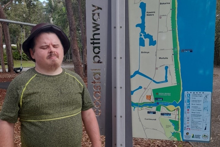 A man with a beard, wearing bucket hat, standing next to a map.