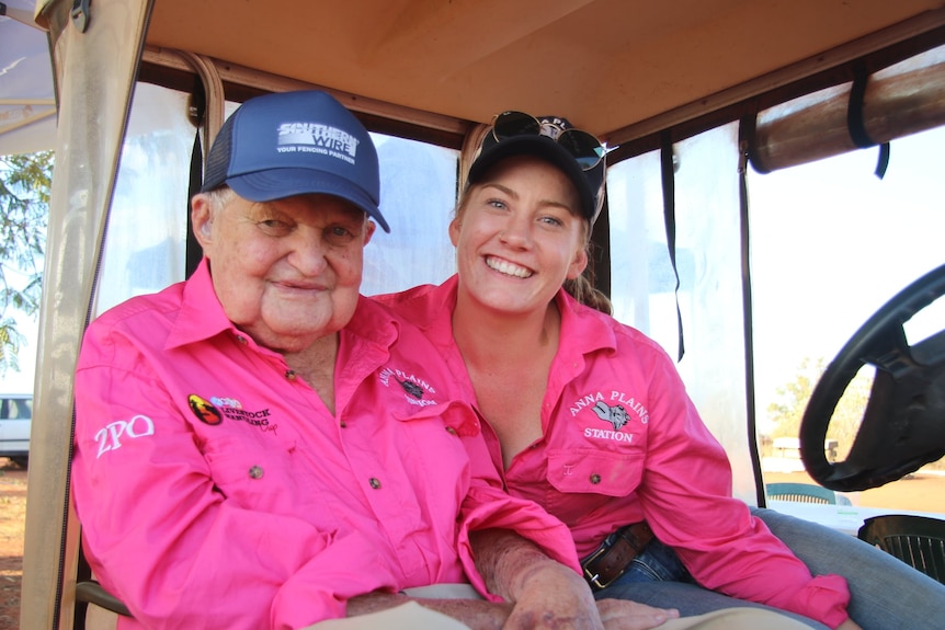 An old man and young woman sitting in a buggy wearing pink shirts