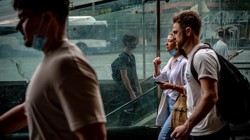 Two young people walk through a train station wearing face masks.