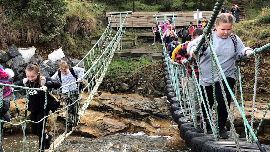 Kids cross a swinging bridge over a fast flowing river.