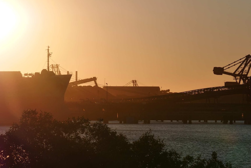 The sun sets over a harbour with large cargo ships.