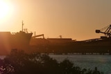 The sun sets over a harbour with large cargo ships.