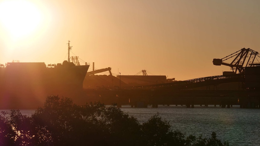 The sun sets over a harbour with large cargo ships.