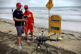 Two lifesavers stand next to a large drone on a beach